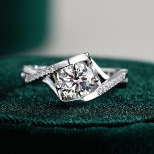 1ct round moissanite engagement ring with twisted split shank band and pavé side stones on silver setting, close-up bridal jewelry on green background